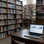 Biblioteca universitária com livros científicos e análise de dados em laptop